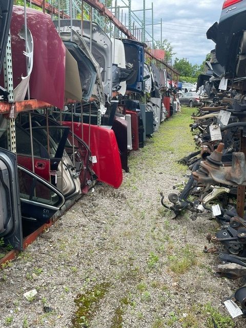 Rows of salvaged car body parts, including hoods and doors, are neatly organized on industrial metal shelving in a lot.