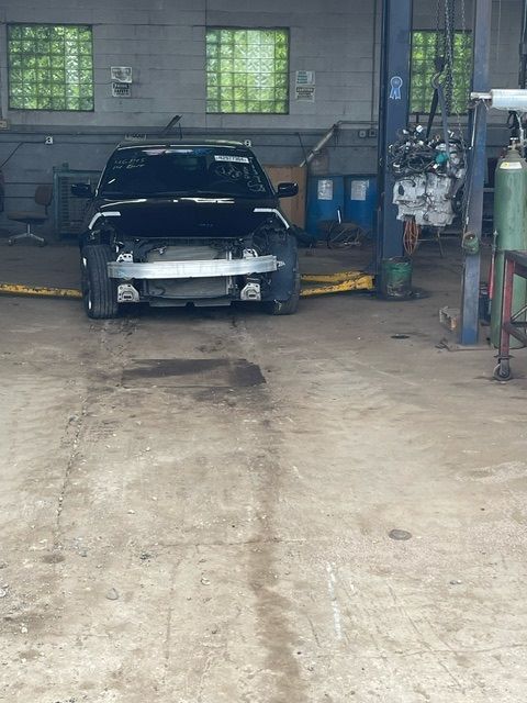 A black car with its front bumper removed sits on a lift inside a car repair garage.