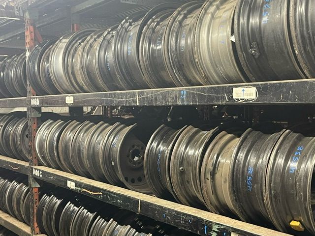 Metal wheels for vehicles neatly organized and stacked on dark industrial storage shelves.