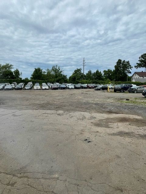 A wide outdoor lot filled with rows of parked cars under a cloudy sky.