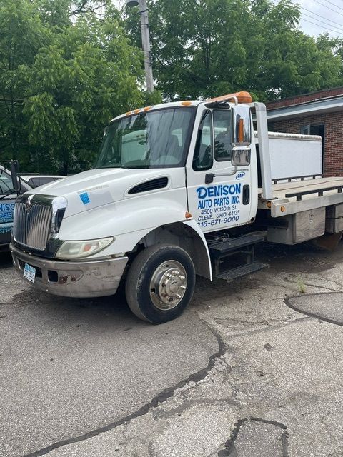 A white flatbed tow truck from Denison Auto Parts parked on an asphalt lot with trees in the background.