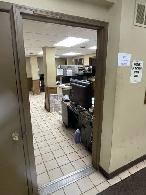 A view into a carpeted office space with cubicles, a black computer monitor on a desk, and tiled flooring.