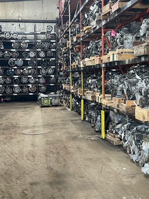 A warehouse interior featuring rows of industrial shelving stocked with numerous automotive engines and transmissions.