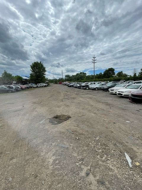 A vast, unpaved parking lot filled with numerous parked cars under a cloudy, overcast sky.