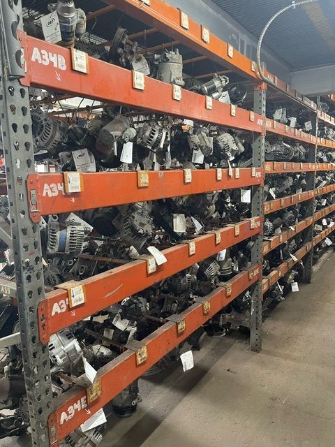 A warehouse shelving unit with orange racks packed with various automotive parts and labeled containers.