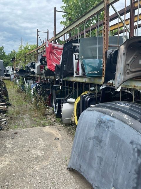 A salvage yard with car hoods and doors stored on metal shelving racks outdoors on an overcast day.