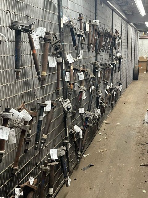 A grid wall in an industrial storage area holding rows of various used automotive struts and mechanical parts.