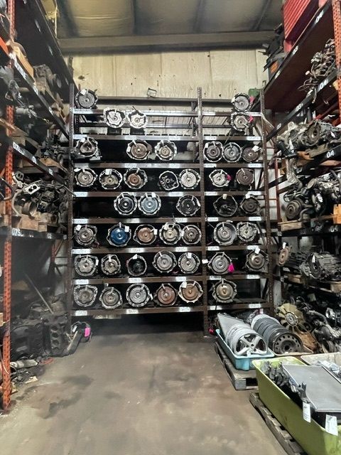An industrial warehouse storage rack filled with numerous automotive transmissions, viewed from a center aisle.