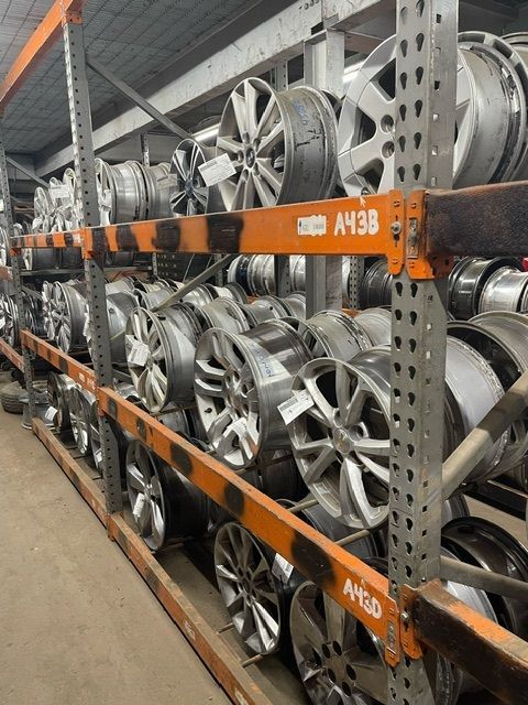Rows of silver automotive wheels stacked on industrial metal shelving in a warehouse.