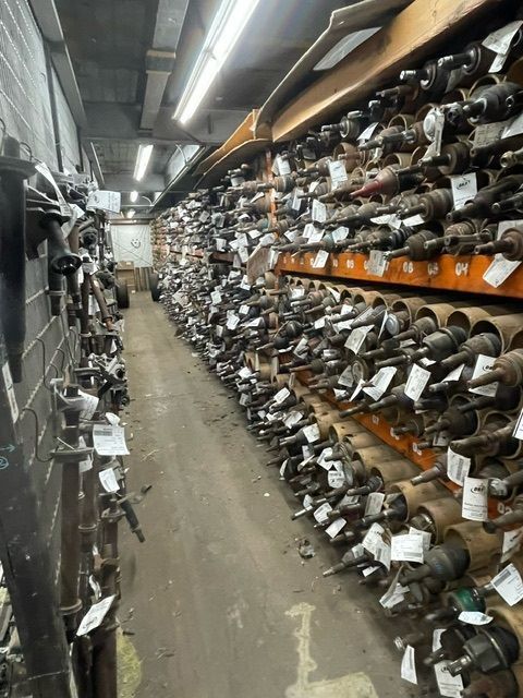 A narrow aisle in an automotive warehouse with shelves stocked with many rows of car axles and metal parts.