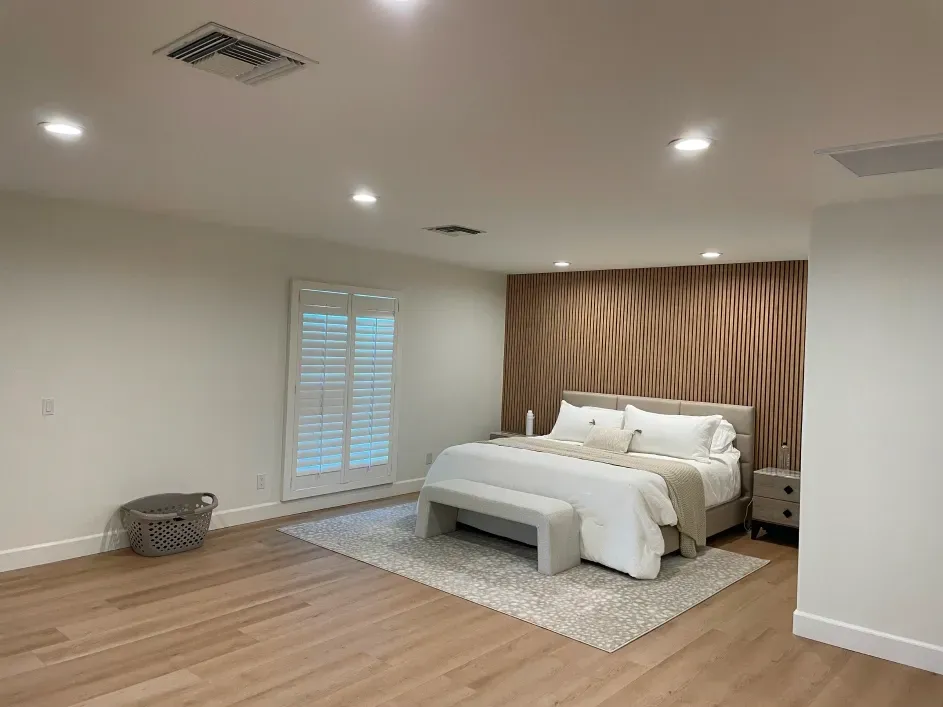 A minimalist bedroom with light hardwood floors, a white bed on a textured rug, and a curved wood-panel accent wall.