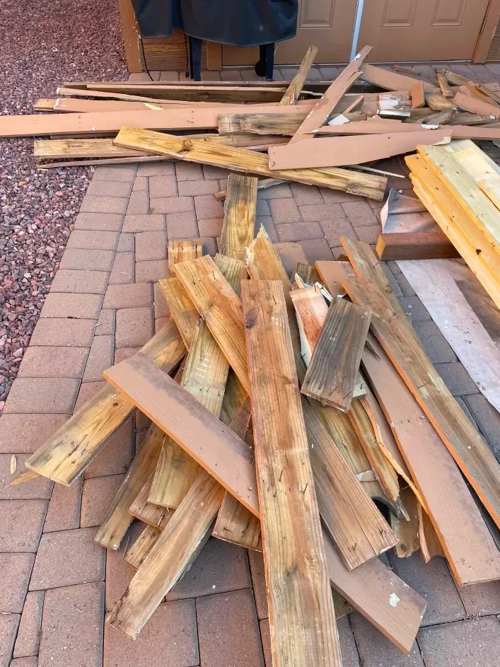 A pile of assorted, weathered wooden boards and construction scrap discarded on a red brick patio.
