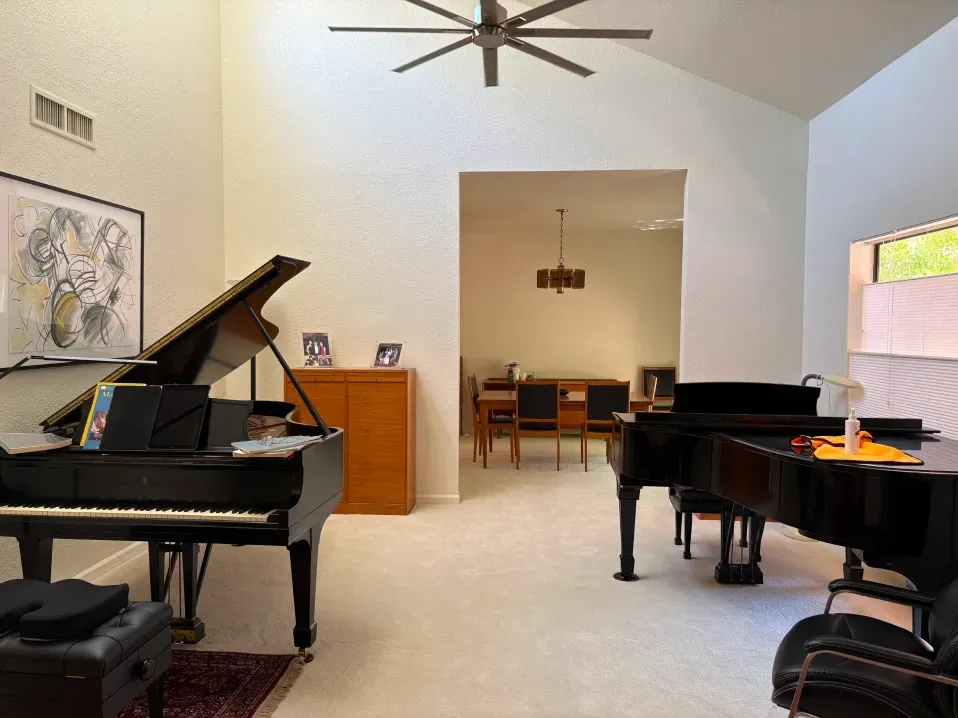 A spacious room with two black grand pianos, a wooden cabinet, and a view into a dining area with a table and chairs.