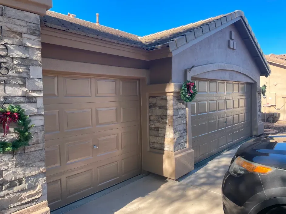 Two tan garage doors on a house with stone accents, decorated with festive Christmas wreaths.