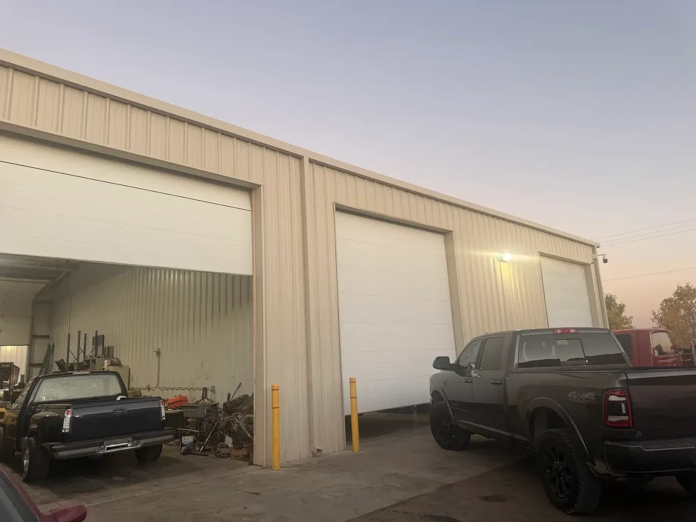 Exterior view of a metal building with two garage doors partially open. Trucks are parked outside.