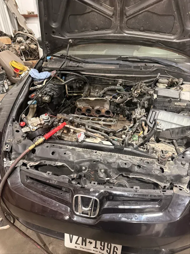 Open car hood revealing engine bay, being cleaned with a spray nozzle. Honda emblem visible.