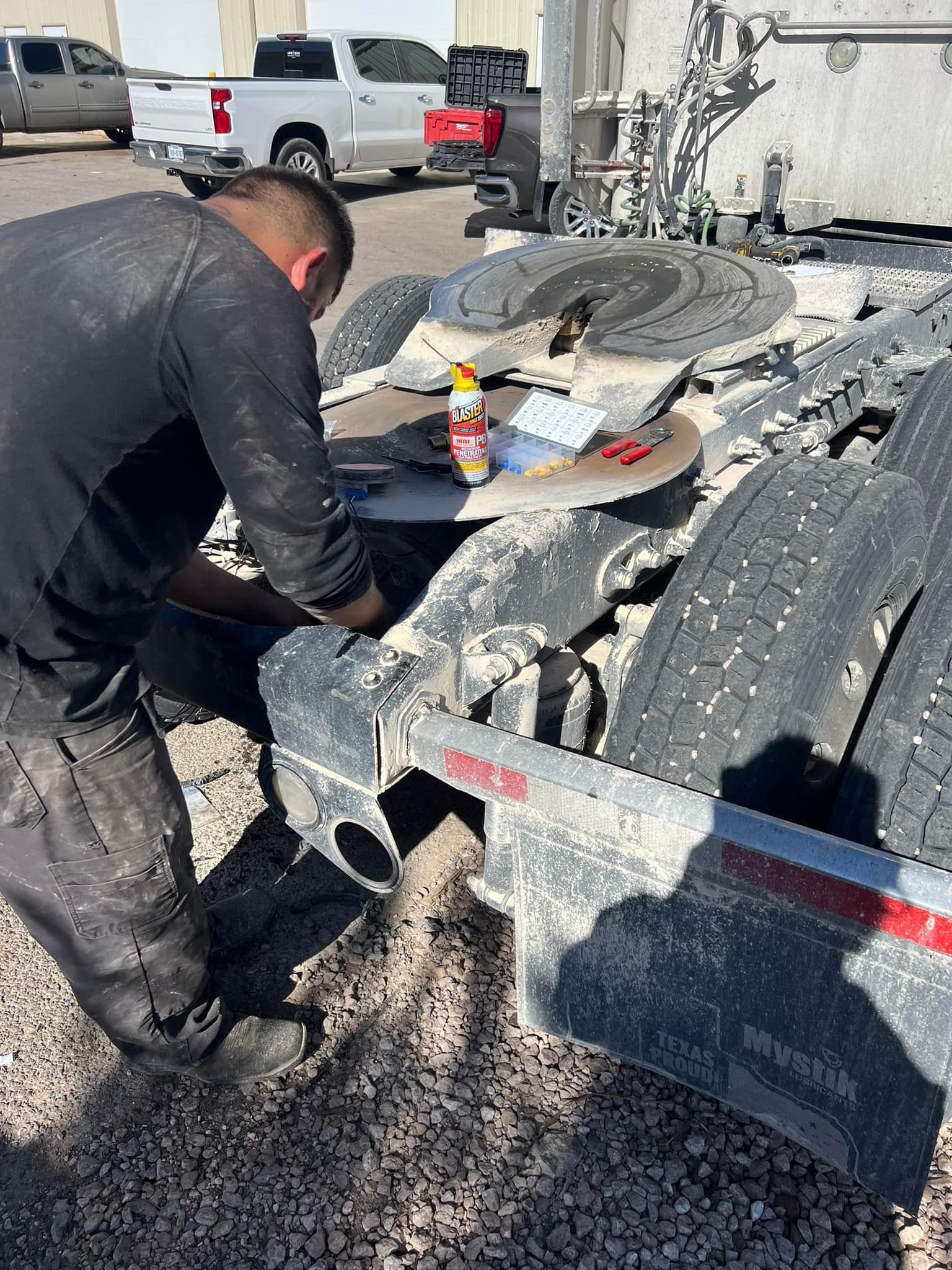 Man working on the undercarriage of a semi-trailer in an outdoor setting.