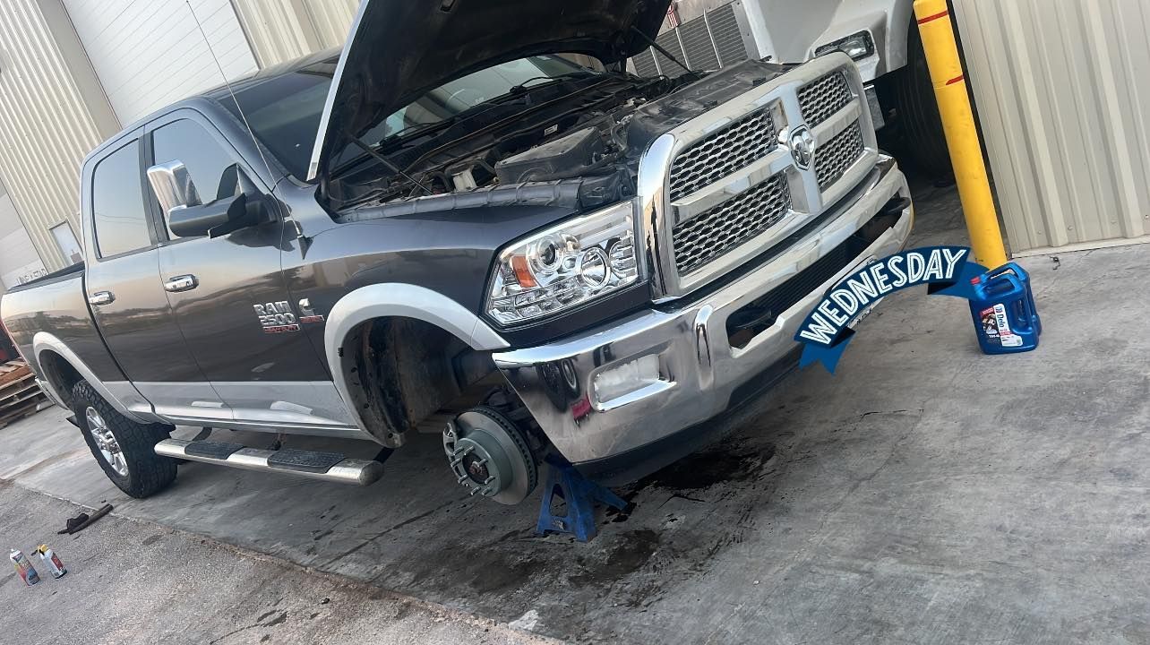 A black pickup truck with its hood open and a missing front tire, possibly being worked on outdoors.