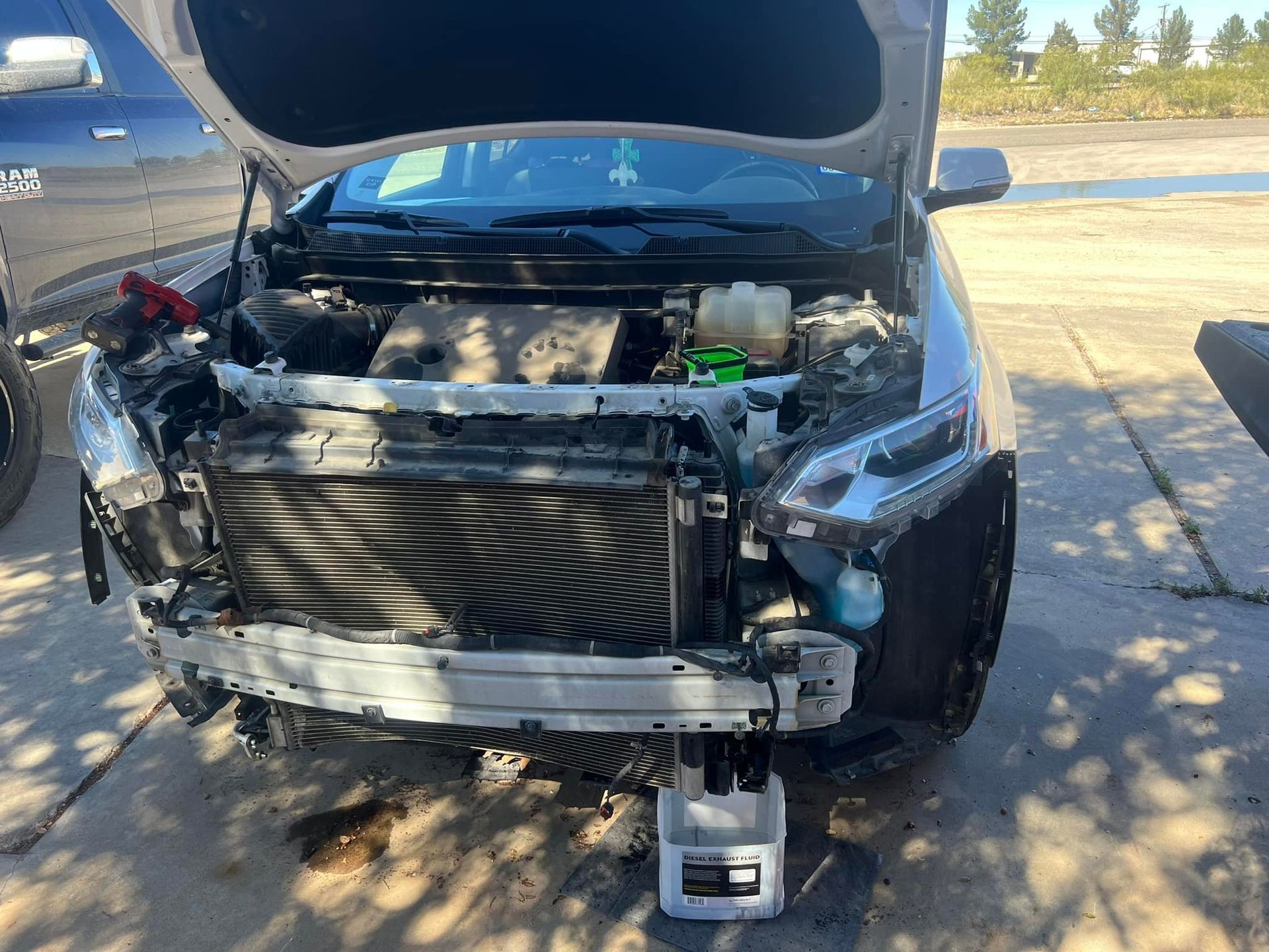 Car with open hood; front end appears damaged, radiator exposed, coolant container below.