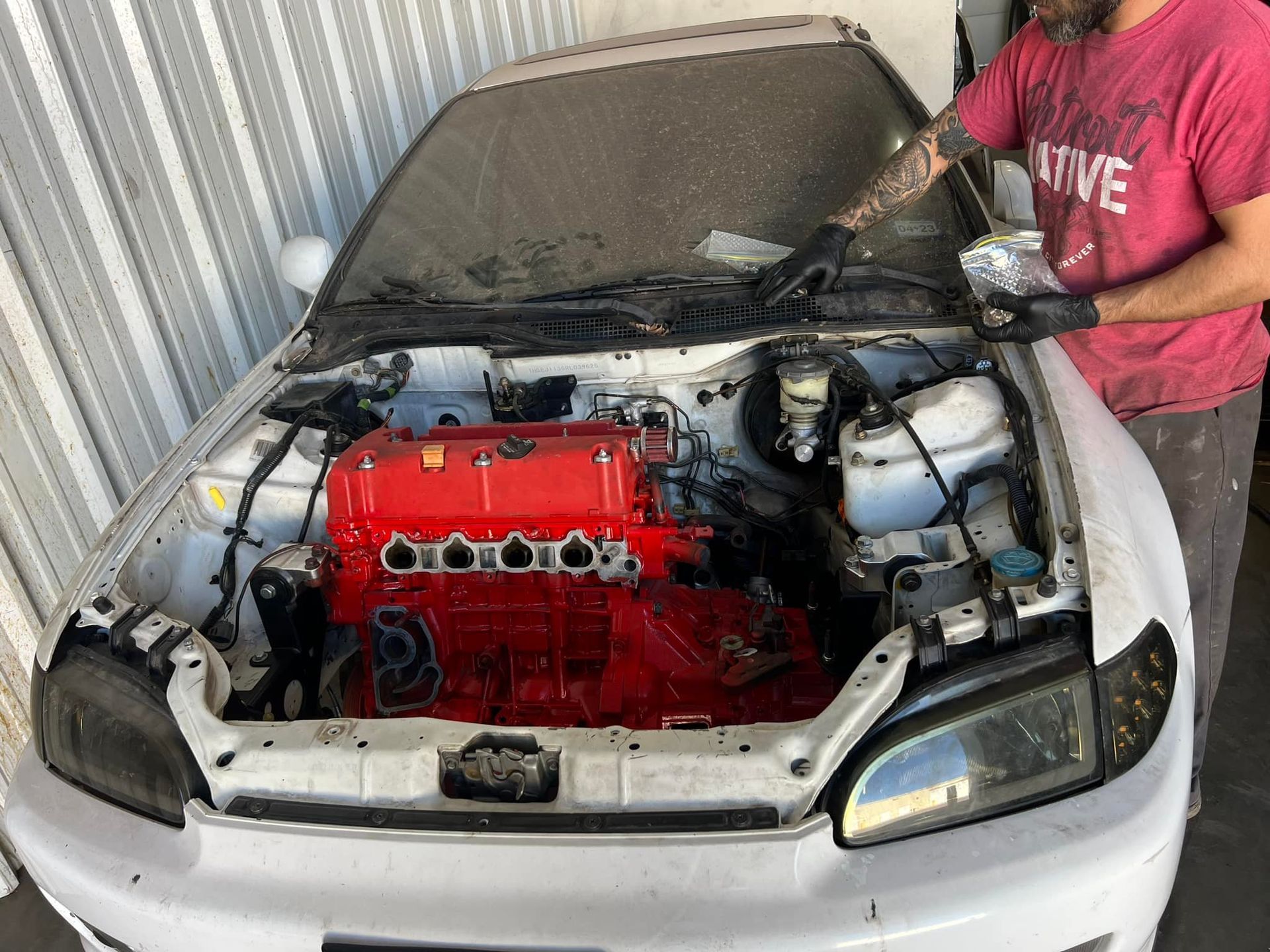 Person working on a white car with a red engine in a garage.