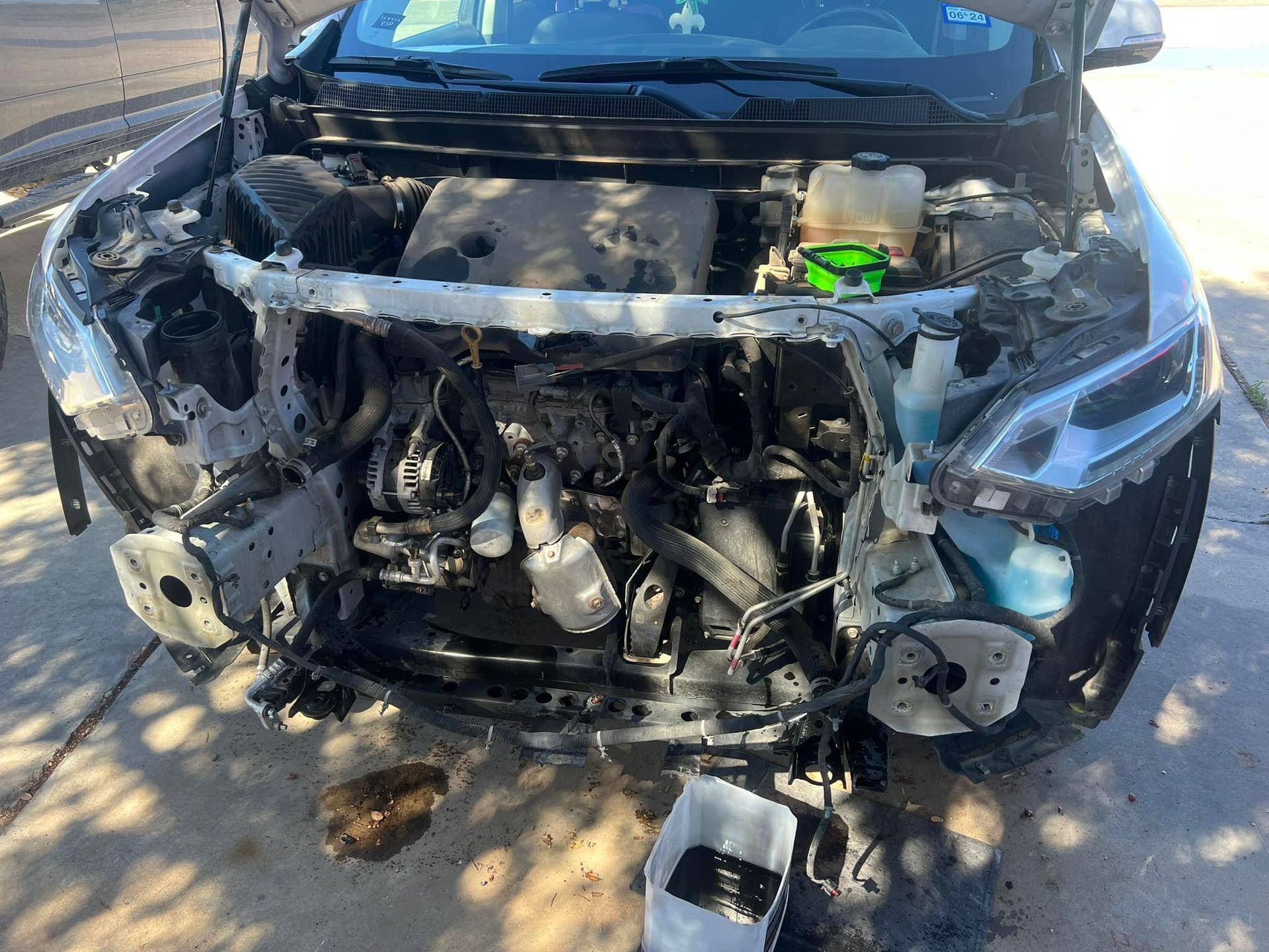 Car with significant front-end damage, exposing the engine compartment. Debris and parts scattered around.