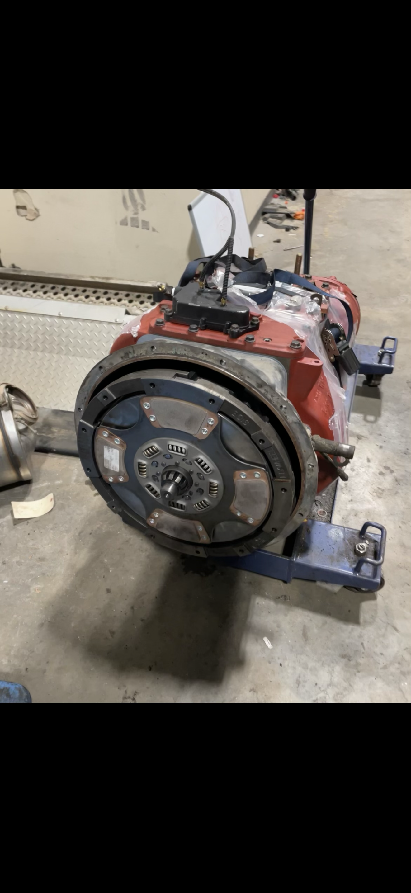A truck transmission with a large clutch assembly, on a blue stand in a shop.