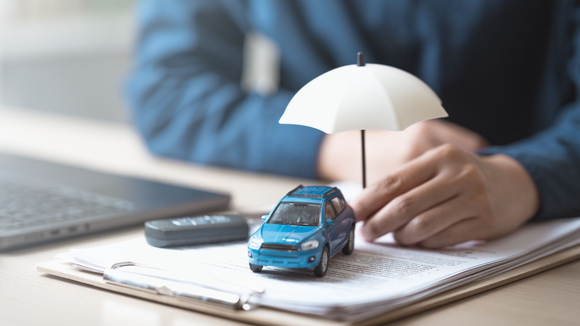 Auto insurance coverage represented by a miniature car, keys, and protective umbrella.