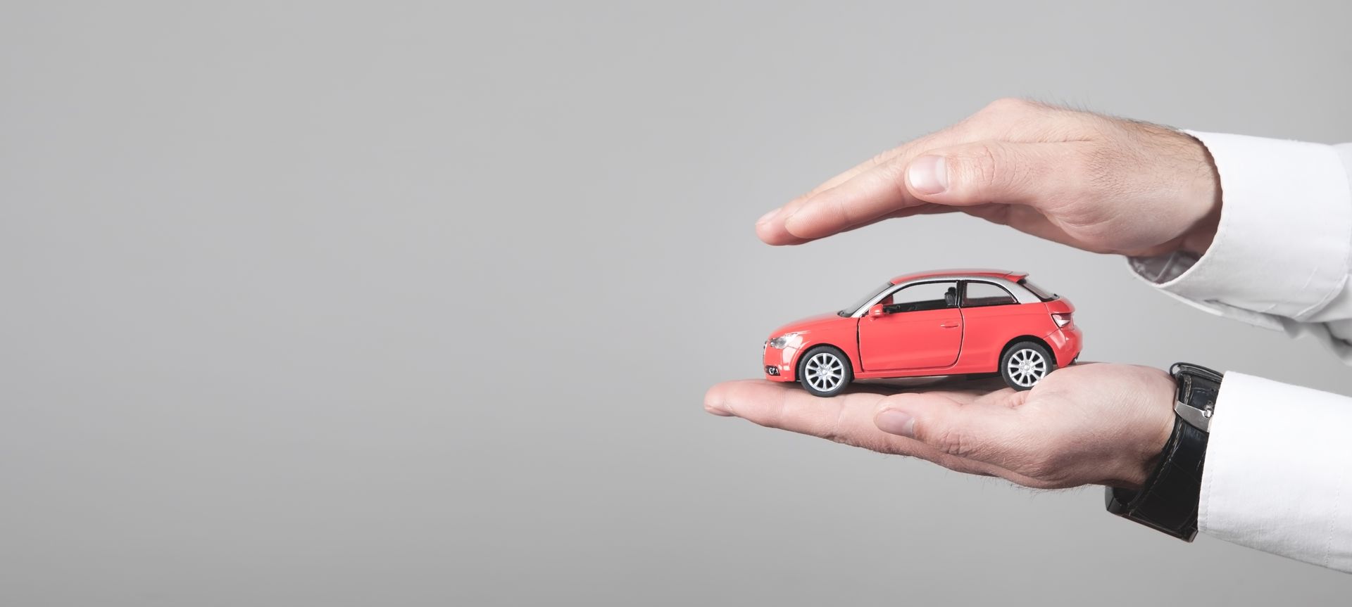 Hands gently holding and protecting a small red car model, symbolizing auto insurance.
