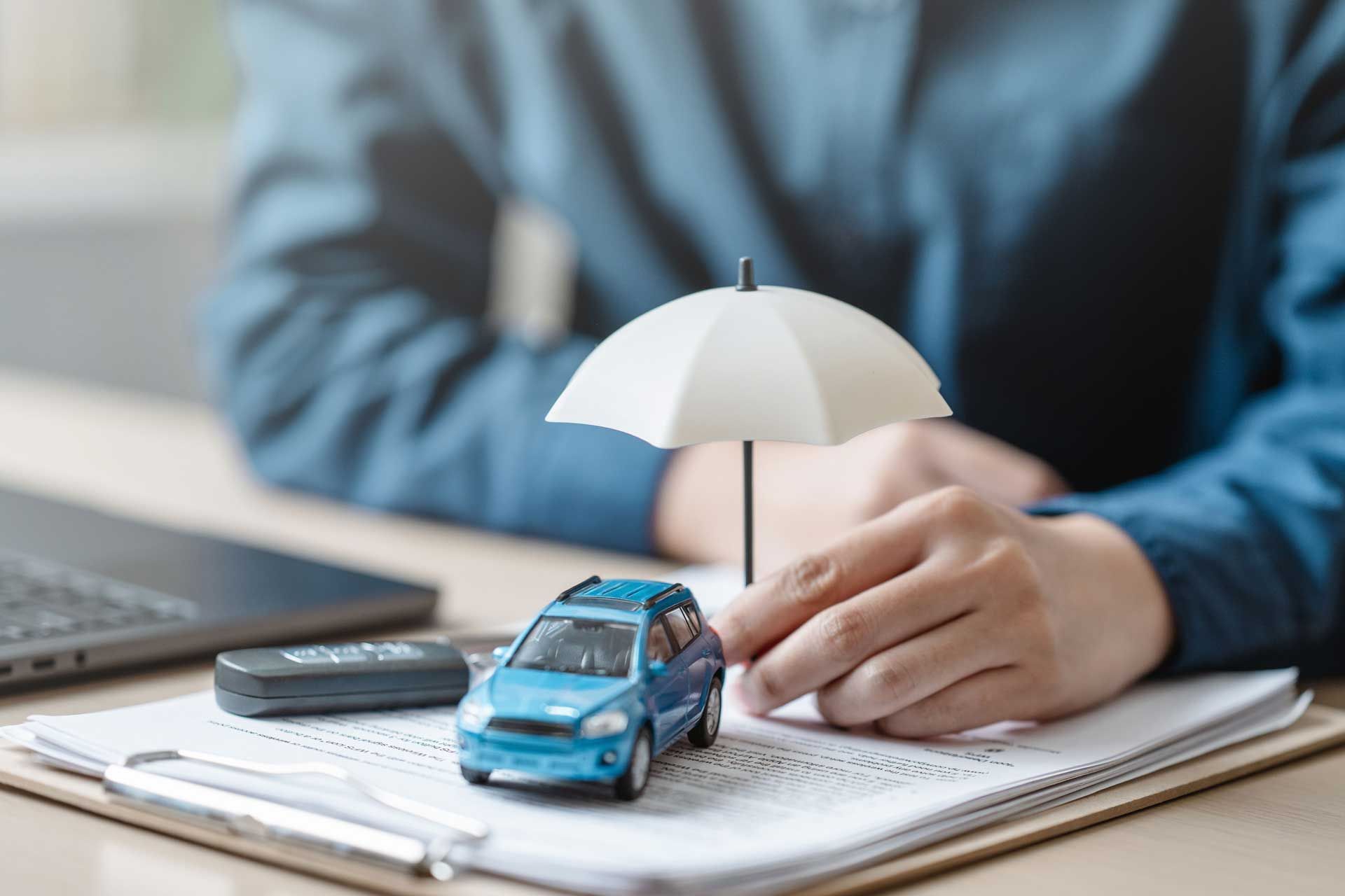 A person is holding an umbrella over a blue car for a car insurance concept. A person is holding an umbrella over a blue car for a car insurance concept.