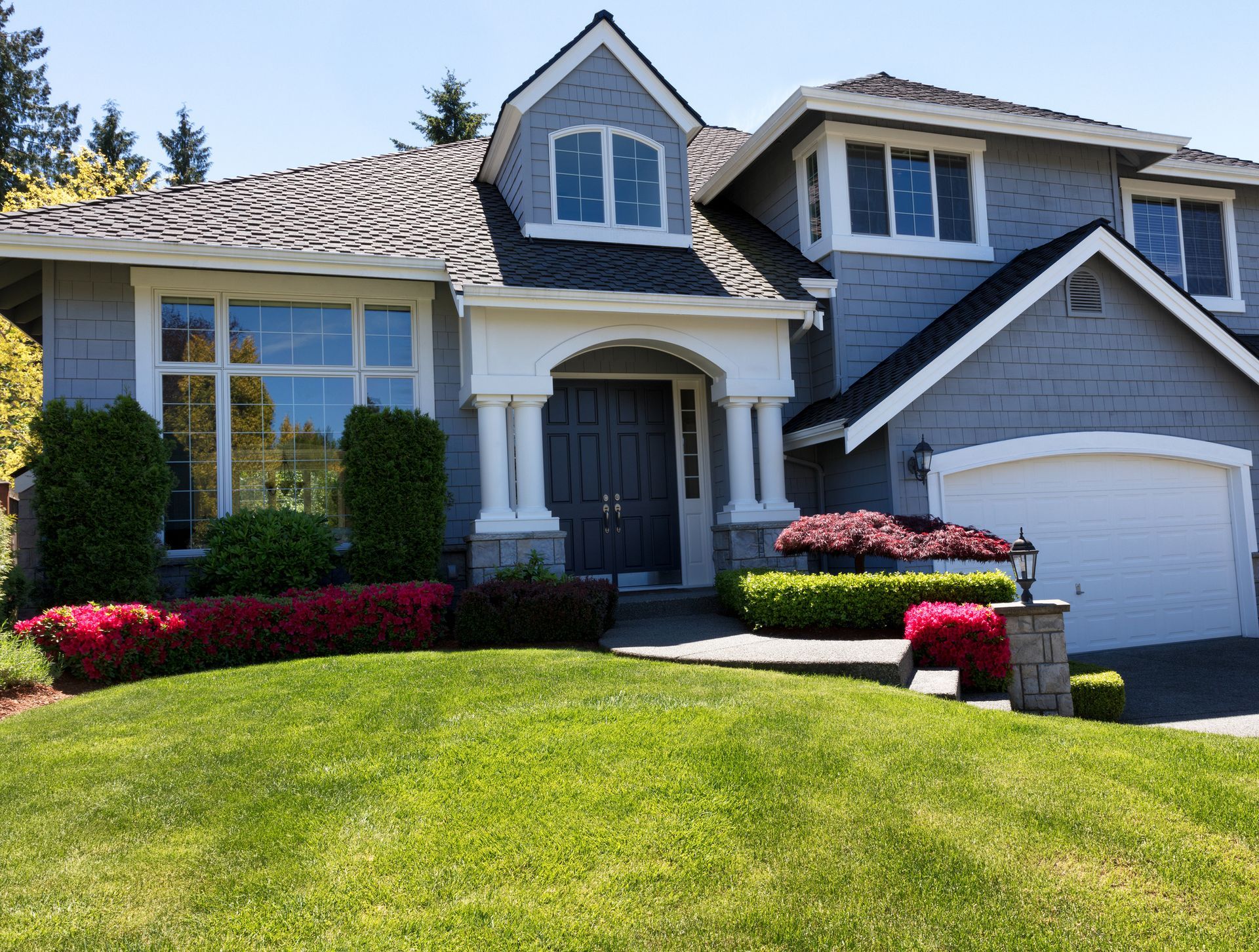 Gray house with white trim, green lawn, and colorful landscaping.