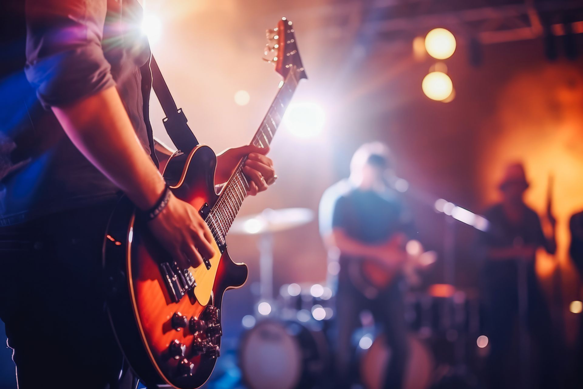 Guitarist on stage, playing, bright lights, band in the background.