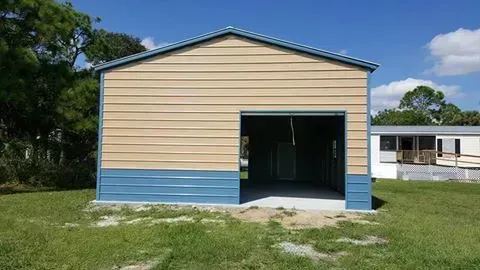 A metal garage with a blue trim is sitting in the middle of a grassy field.