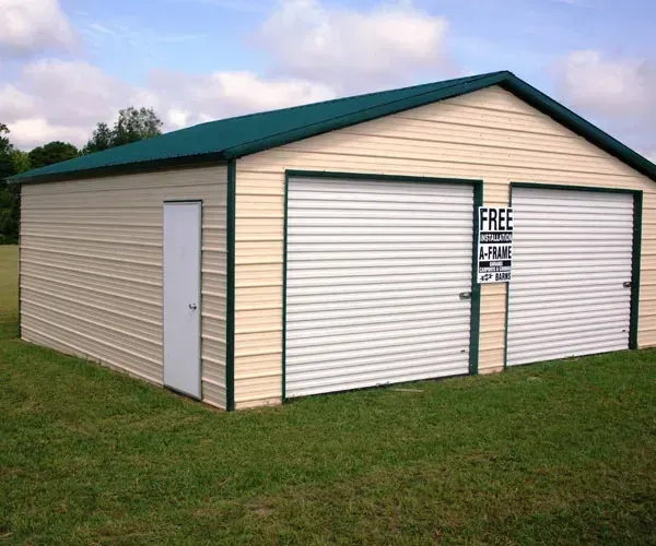 A metal garage with two garage doors and a green roof is sitting in the middle of a grassy field.