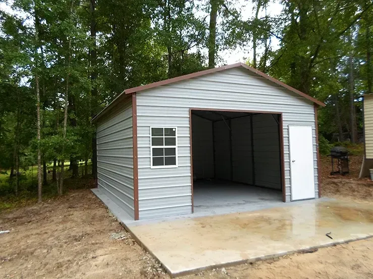 A metal garage with a window and a door is sitting in the middle of a dirt field.