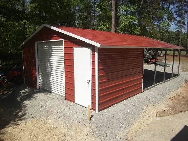 A red metal garage with a white door is sitting on top of a gravel driveway.