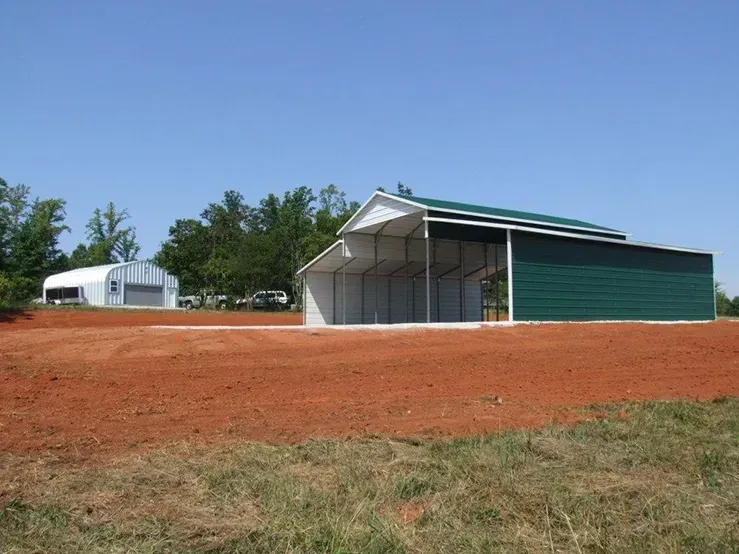 A green and white barn is sitting in the middle of a dirt field.