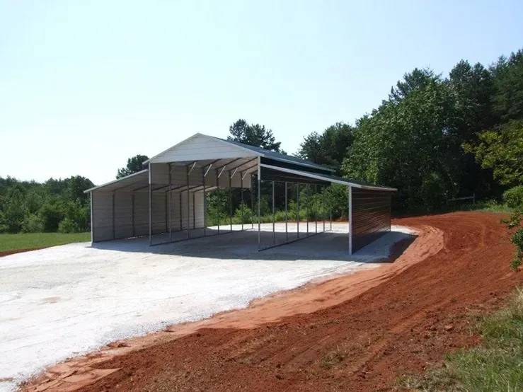 A large metal building is sitting on the side of a dirt road.