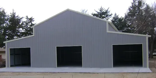 A gray building with three garage doors and trees in the background