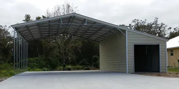 A metal garage with a canopy over it is sitting next to a house.