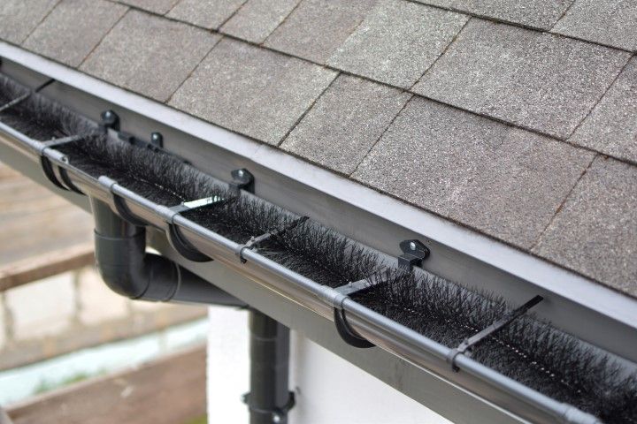 Leaf guard gutter attached to a house roof edge, with downspout visible underneath.
