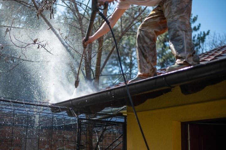 Person on a roof spraying water over a yellow house on a sunny day