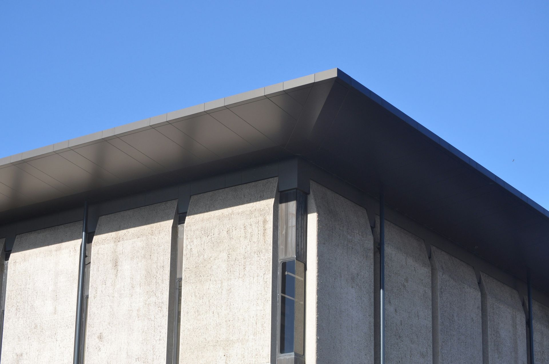 Close-up of a modern building roof and gray textured wall against a blue sky