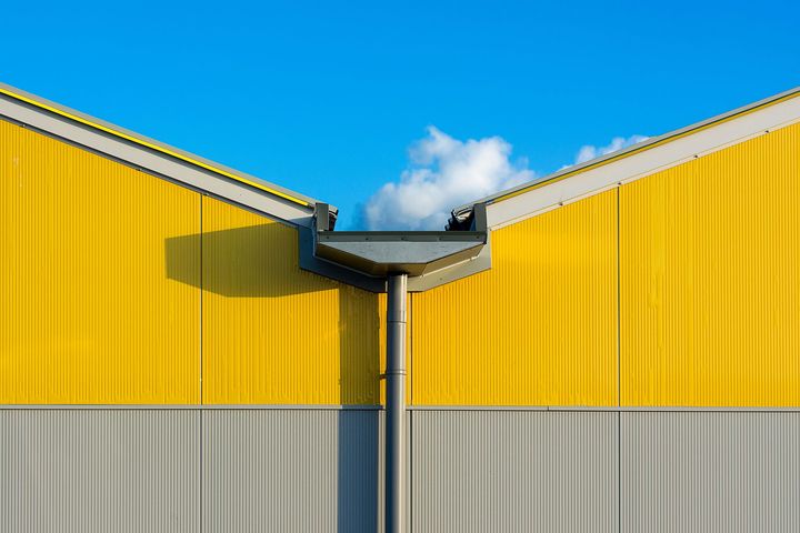 Yellow and gray industrial building facade with a central roof junction under a blue sky