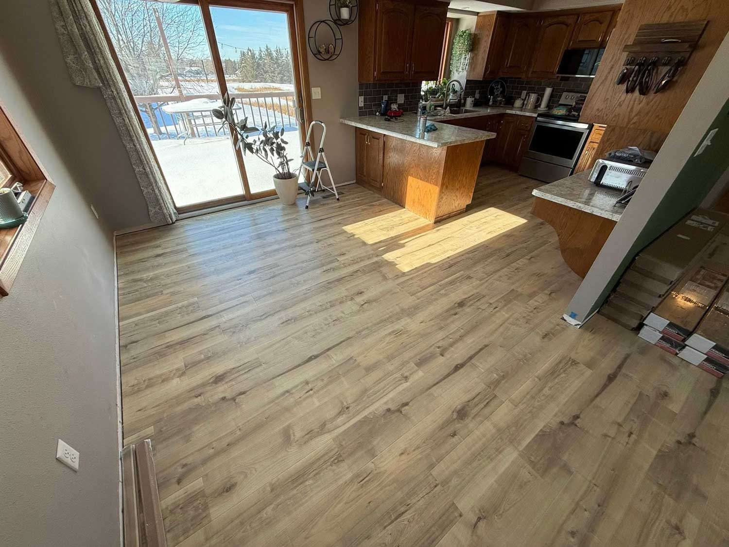 Wooden floor interior with a kitchen, dining area, and large window overlooking a snowy landscape.