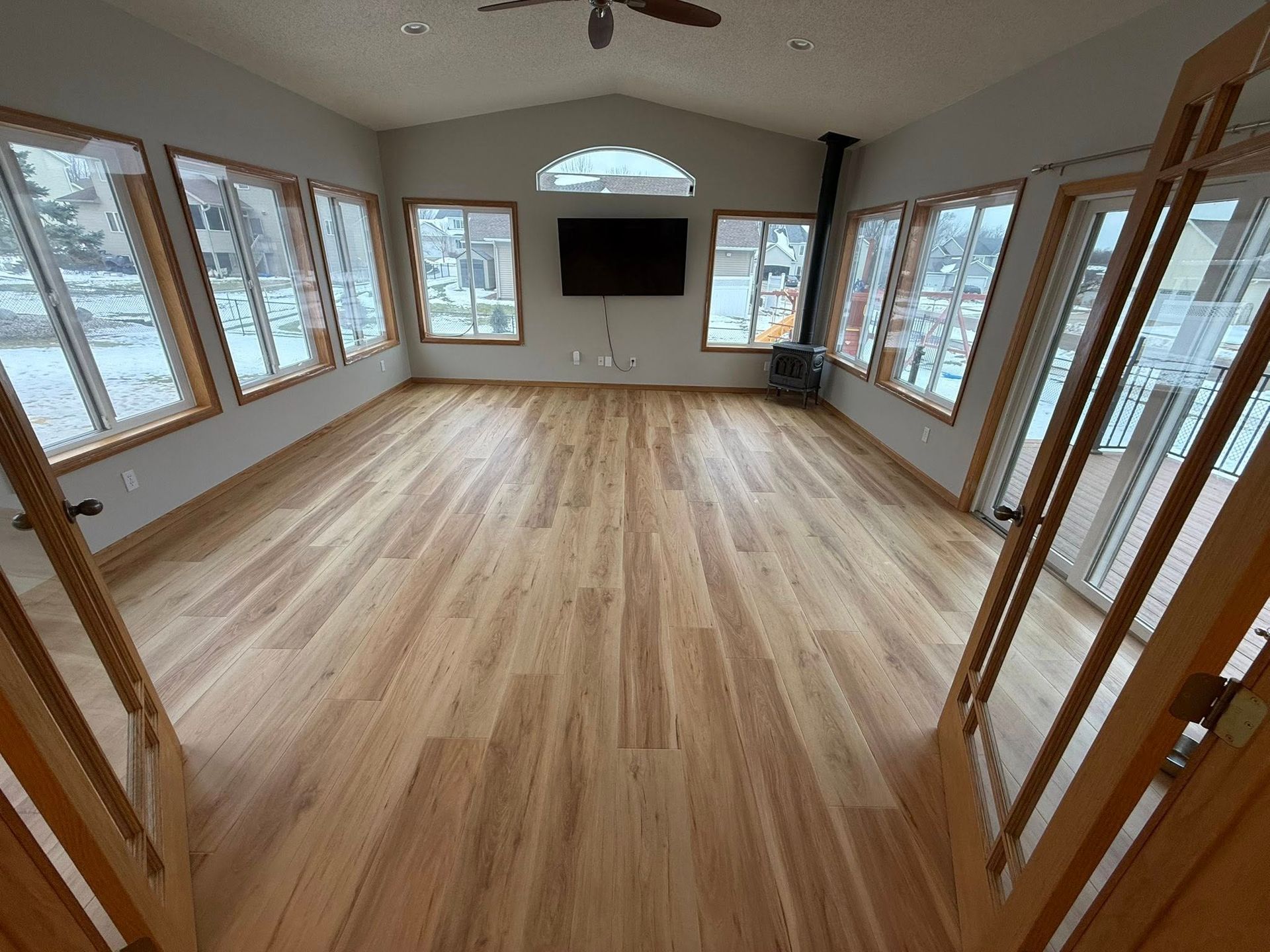 Sunroom with wood floors, numerous windows, mounted TV, and wood-framed doors.
