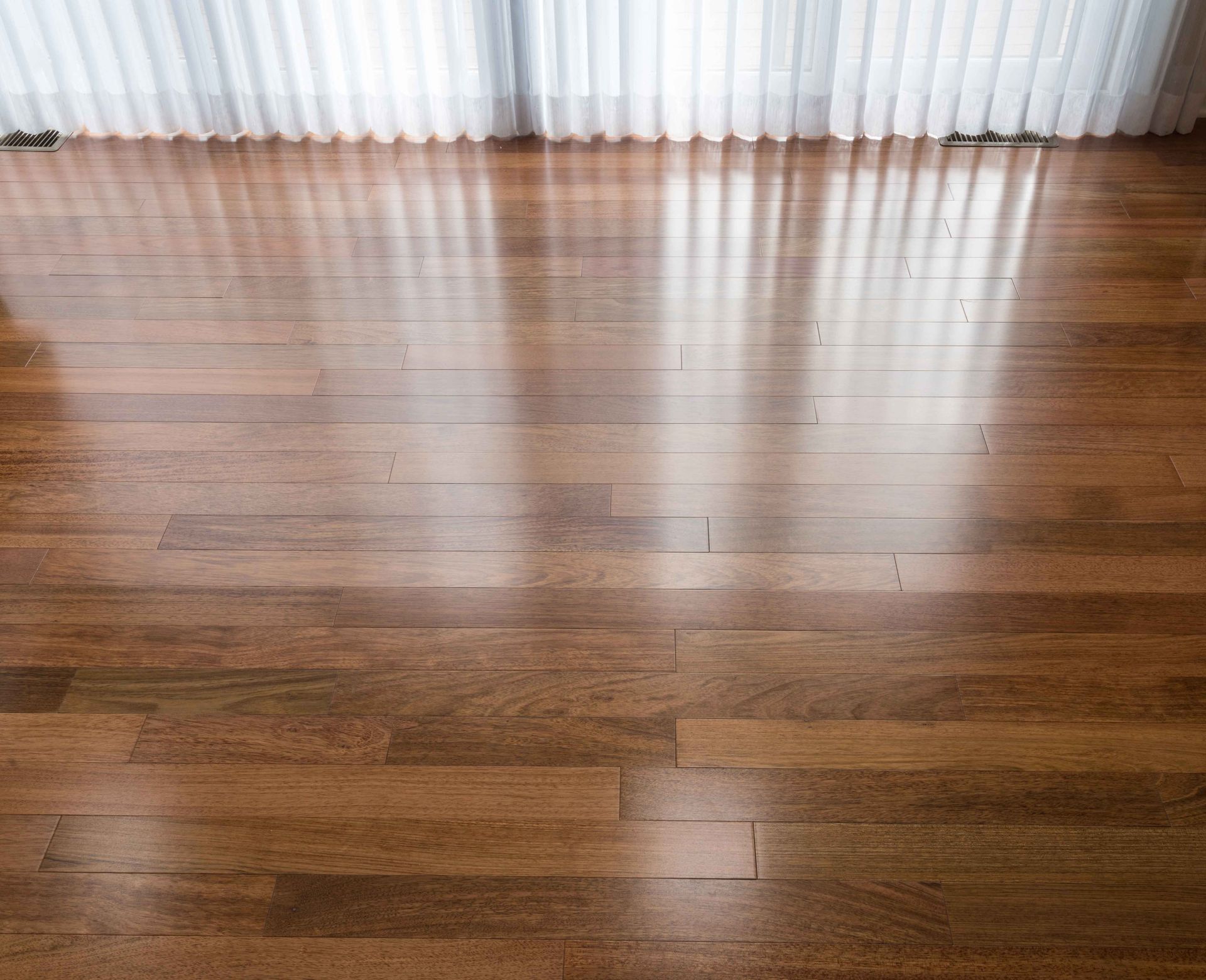 Shiny, brown hardwood floor reflecting light from sheer white curtains.