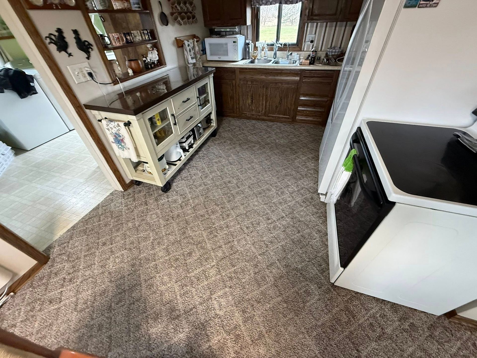 Kitchen with brown cabinets, carpet, appliances, and a glass-doored cabinet.