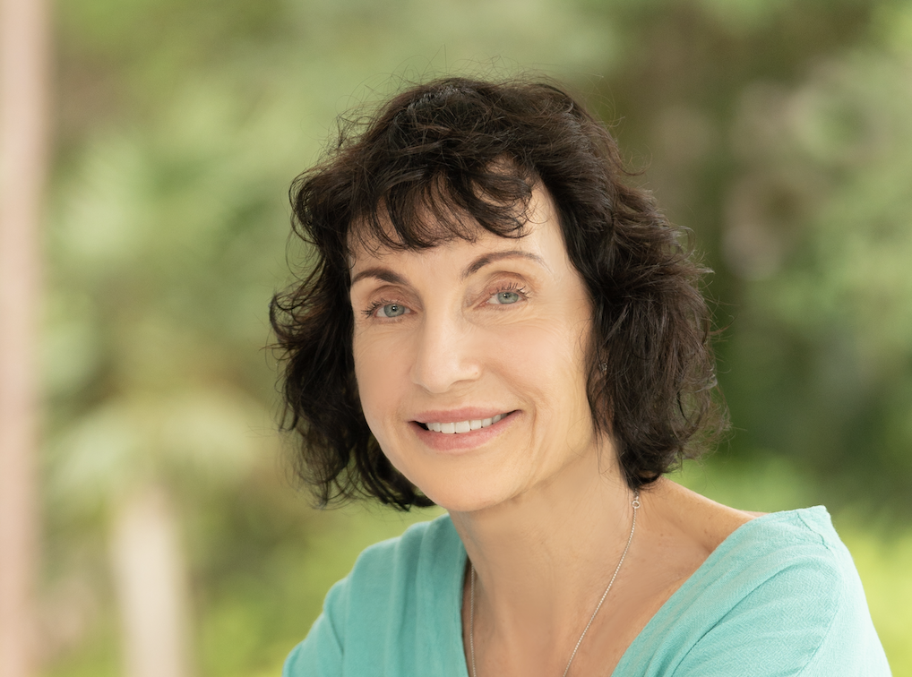 Smiling woman with dark curly hair in a light blue top against a blurred green background. Photo of Helen Jessup Murray