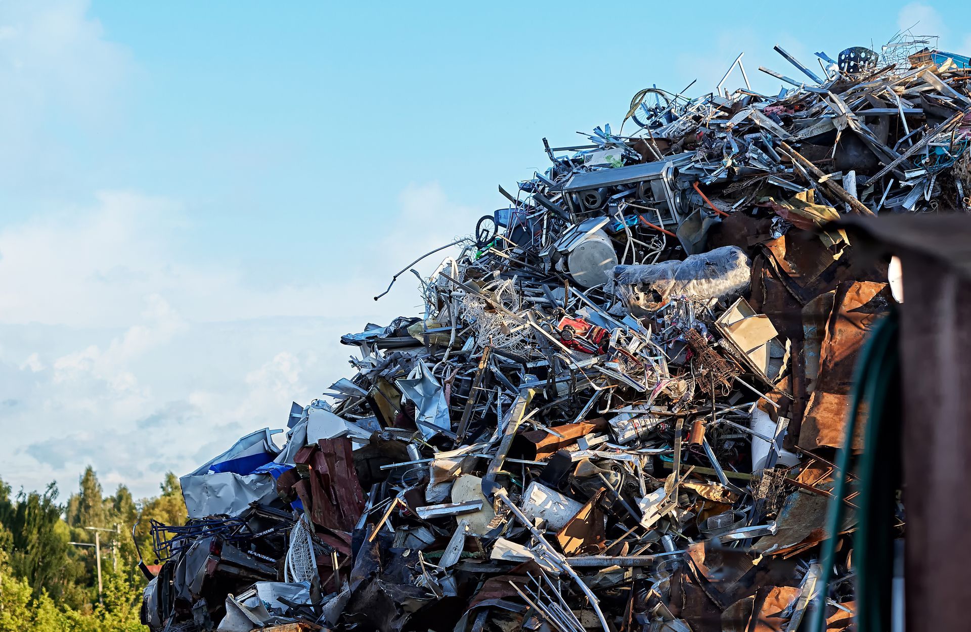 A large pile of scrap metal consisting of various materials and green foliage in the background. A large pile of scrap metal consisting of various materials and green foliage in the background.