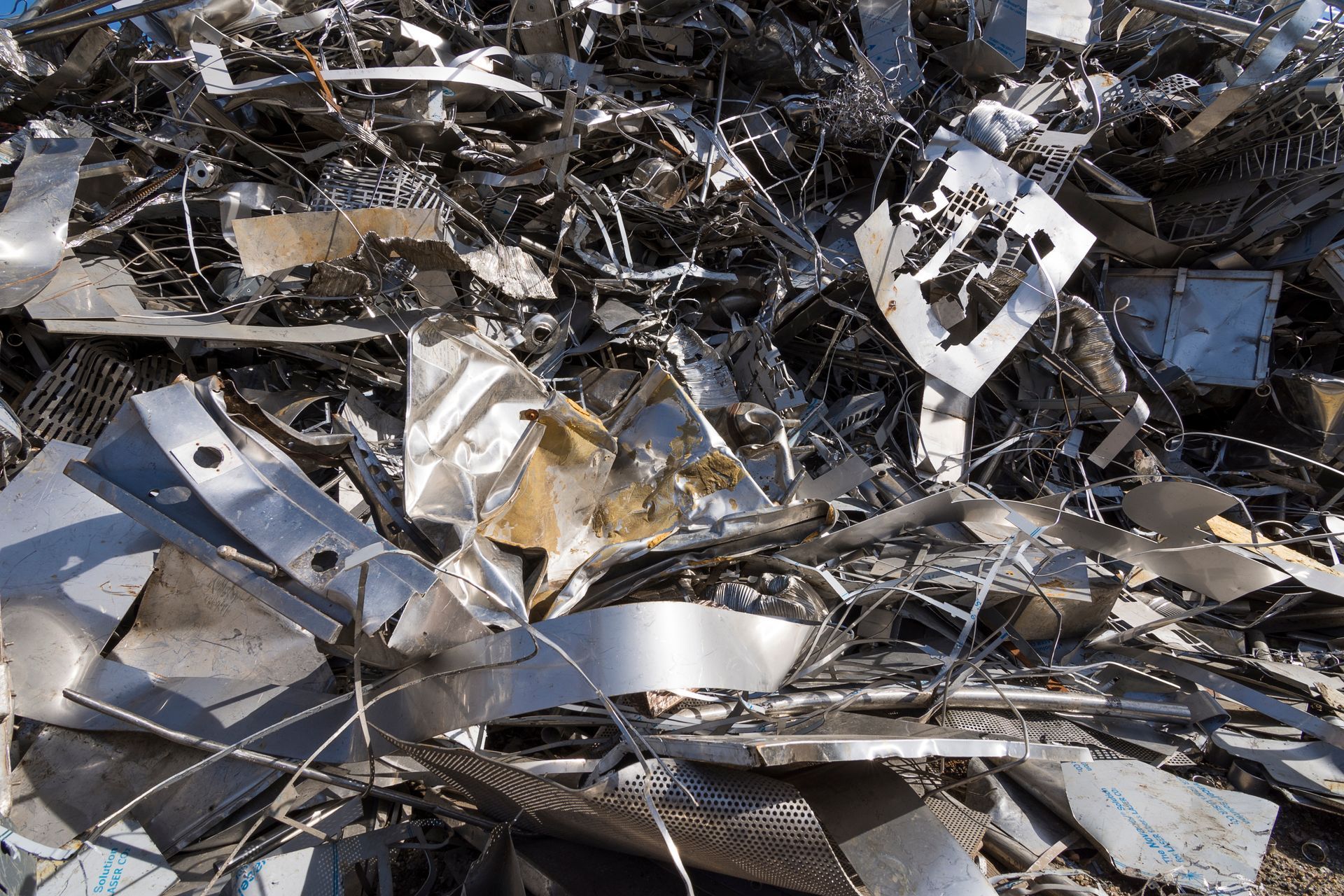 A green JK Recycling crane stands besides a large pile of scrap metal in an industrial setting. Metal Recycler